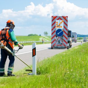 20179092 - road landscapers cutting grass around mileposts along the road using string lawn trimmer